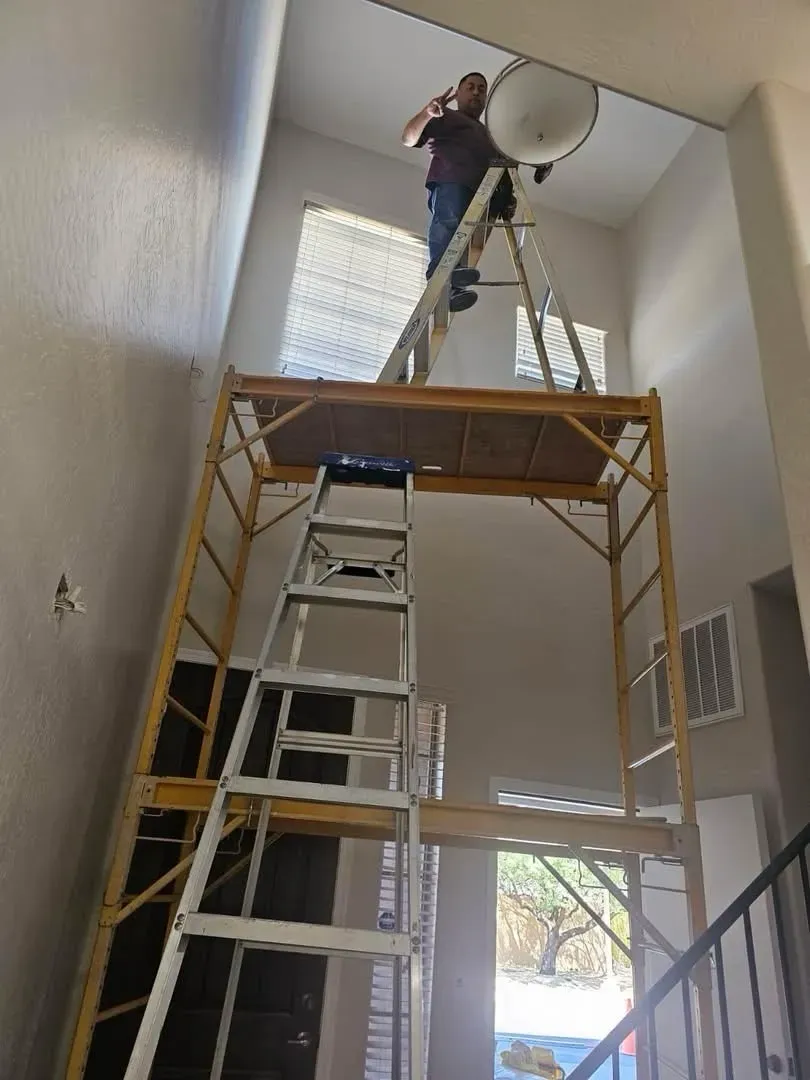 Electrician on scaffolding installing a high ceiling light fixture - Orozco Electric